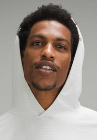 Weißer Hoodie mit einem strukturierten Muster und einer angenähten Kapuze. Glattes Stoffdetail am Kragen und an den Schultern. Deutliche Gesichtszüge.