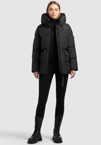 Crni puffer jakna s kapuljačom, s prednim patentnim zatvaračem, elastičnim pojasom u struku i dva bočna džepa. Nosena s crnim tajicama i vojnim čizmama.