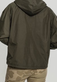 Hoodiejacka i mörk olivfärgad tyg med en lätt och slät textur. Har sänkta axlar och en elastisk nederkant. Matchas med beige kamouflagedetaljer.