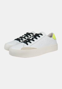 Sneaker bianche con lacci neri, accenti in suede e un tab sul tallone giallo fluo. Parte superiore in pelle liscia, punta rotonda e suola platform.