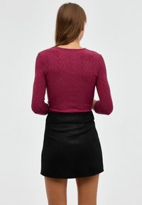 Top de punto burdeos con mangas largas y un patrón de diamantes, combinado con una minifalda de ante negra. Se muestra la vista trasera.