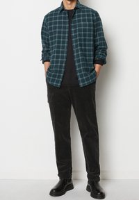 Koszula flanelowa w ciemnym odcieniu teal z jasnoniebieskim wzorem w kratę, zapięta na guziki; połączona z czarnymi spodniami sztruksowymi i czarnymi botkami na kostkę.