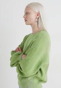 Grønn oversized genser med ribbestruktur. Lange ermer og rund hals, brukt med sølv hoops. Nøytral bakgrunn.