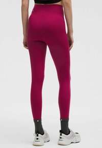 Fuksjowe legginsy z wysokim stanem i elastycznym materiałem, podkreślające nogi. W połączeniu z szarymi skarpetkami do kostek i białymi trampkami.