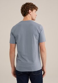 Svijetloplava kratka majica s kratkim rukavima od mekog materijala s okruglim izrezom, prikazana na modelu okrenutom leđima, u kombinaciji s tamnim trapericama.