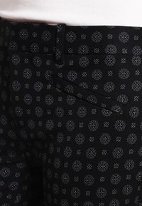 Černé kalhoty s geometrickým vzorem v šedé barvě, s úzkým střihem a detaily přední kapsy. Vyrobeno z robustní tkaniny.