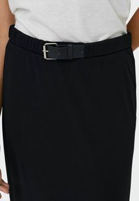 Jupe noire avec une texture lisse, dotée d'une large taille élastique et d'une boucle de ceinture sombre pour le réglage et l'amélioration des détails.