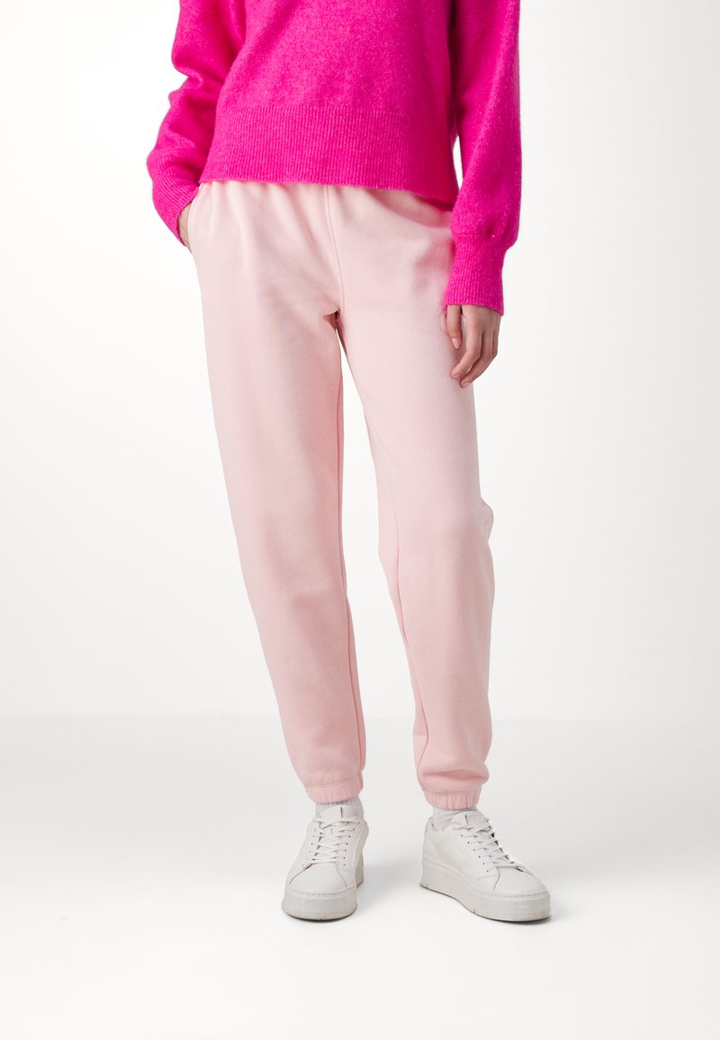 Pantalons de survêtement roses avec une coupe décontractée, taille élastique et poignets côtelés, associés à des baskets blanches et un pull en tricot rose vif.