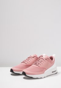 Zapatillas deportivas rosas con parte superior de malla, punta redondeada, entresuela blanca y suela negra. Presenta cordones y una pestaña en el talón.