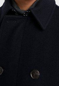 Abrigo de mezcla de lana en color navy que presenta un diseño de doble botonadura, grandes botones de cuerno y un cuello con muesca. Textura suave con un acabado liso.