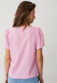 Lyserød bluse med pufærmer, der har et tekstureret hulmønster, firkantet halsudskæring og en afslappet pasform. Bagsiden har en subtil design detalje.