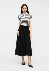 Ριγέ πουκάμισο πόλο με κοντά μανίκια σε λευκό και μαύρο, συνδυασμένο με μαύρη αέρινη μακριά φούστα με ελαστική μέση. Μαύρα παπούτσια με τακούνι.