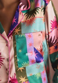 Bunt gemustertes Pyjamashirt aus seidenähnlichem Stoff. Es zeigt verschiedene Farben, darunter Türkis, Rosa und Braun, mit Sternmotiven und kontrastierenden Knöpfen.
