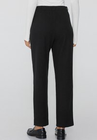 Zwarte elastische taillebroek met een recht model. Gemaakt van zacht materiaal, met een gladde textuur en minimale details.