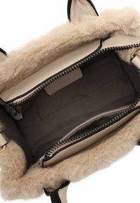 Kleine handtas met een zachte, beige bontvoering en een gestructureerde crèmekleurige leren binnenkant. Voorzien van een zwarte rits en stoffen vakken voor organisatie.