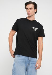 Czarny bawełniany t-shirt z okrągłym dekoltem, z grafiką na klatce piersiowej z napisem "TOMMY JEANS NYC". Miękka tekstura i luźny krój.