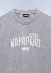 Camiseta de algodón gris con cuello redondo. Presenta un logo en relieve blanco "NAPAPIJRI 1987" y "EST.1987" en la parte frontal. Textura suave.