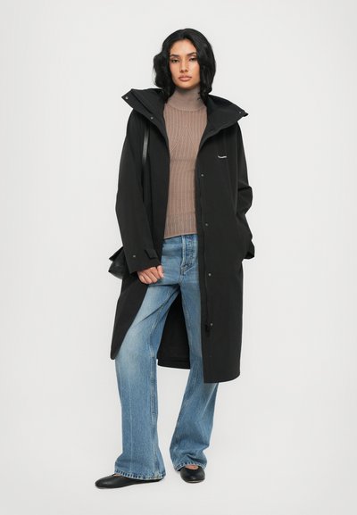 Black waterproof coat with a hood, paired with a brown ribbed knit sweater and light blue wide-leg jeans. Black slip-on shoes complete the outfit.