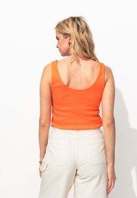 Débardeur orange côtelé à bretelles larges, coupe ajustée et dos en scoop, associé à un pantalon beige clair taille haute avec poches arrière.