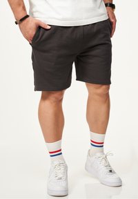 Dunkelgraue Baumwollshorts mit seitlichen Taschen, elastischem Bund und entspanntem Schnitt, kombiniert mit weißen Turnschuhen und gestreiften Socken.