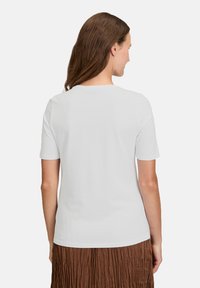 Hvid kortærmet t-shirt lavet af blødt stof, med rund halsudskæring og en glat rygdesign. Båret med en brun plisseret nederdel.