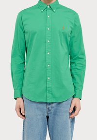 Zelená bavlněná košile na knoflíky s klasickým límcem, dlouhými rukávy a malým vyšitým logem. Obsahuje zakulacený lem a zapínání na knoflíky.