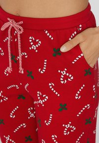 Rode pyjamabroek met een feestelijk patroon van witte suikerstokken en groene hulst. Voorzien van een trekkoord in de taille en zijzakken.