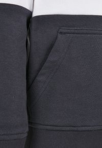 Felpa blu navy con una striscia bianca, dotata di tasca a marsupio frontale e polsini e orlo a coste. Materiale in cotone morbido e testurizzato.