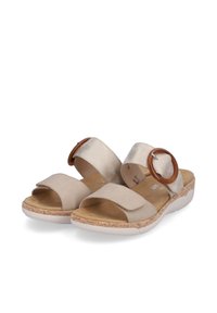 Sandales beiges avec deux larges brides ; l'une a un accent circulaire. Semelle texturée imitant un motif tissé. Talon bas et rembourré pour le confort.