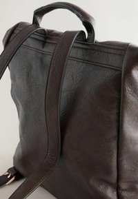 Sac à dos en cuir marron avec une texture lisse, une poignée supérieure courte et des bretelles réglables. Présente des coutures discrètes et un design épuré.