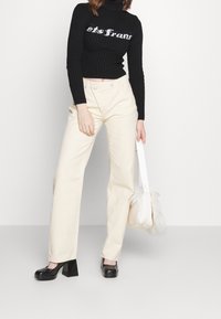 Czarny prążkowany golf z białym napisem, kremowe spodnie o szerokich nogawkach, czarne masywne buty na obcasie oraz biała torebka z futrzanym akcentem.