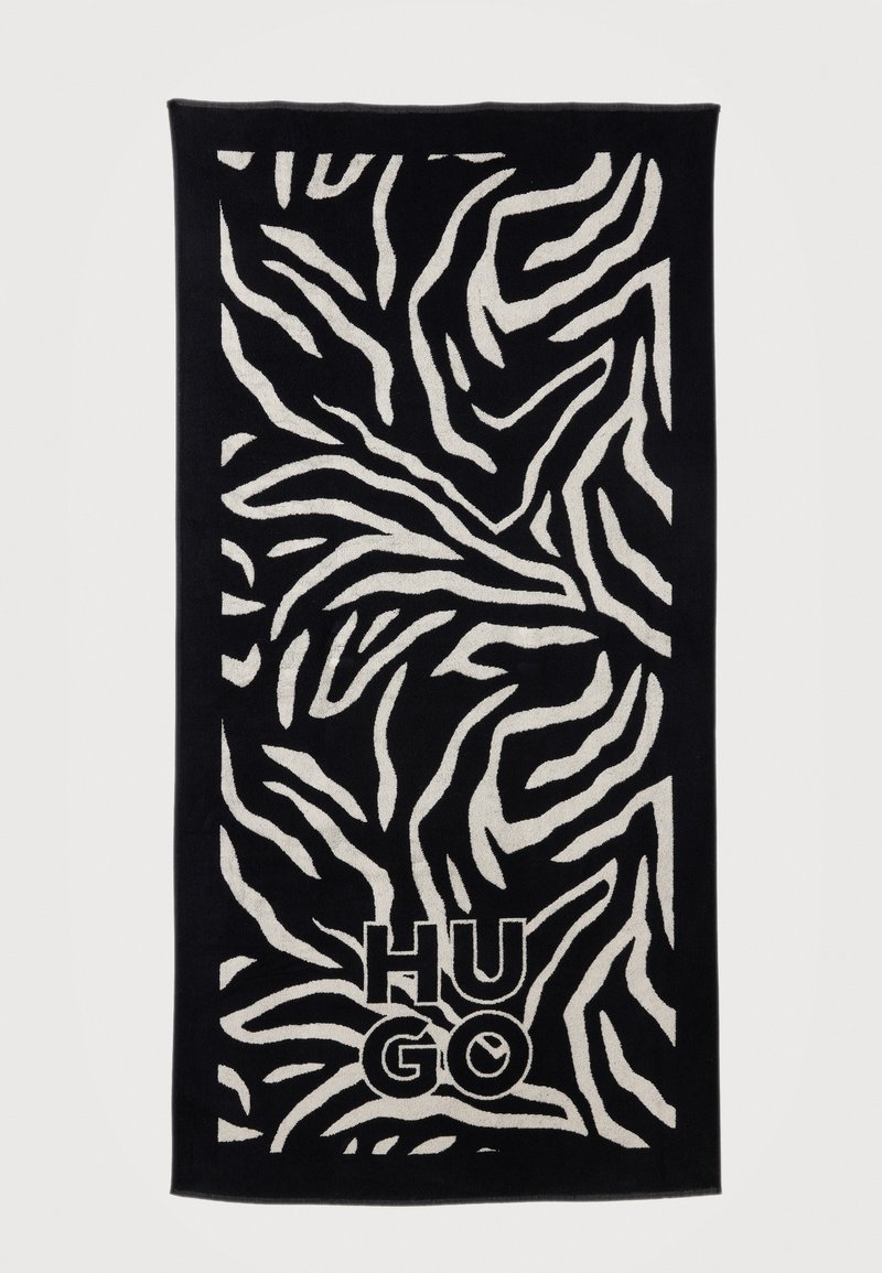 Μαύρη πετσέτα με λευκό σχέδιο ρίγες ζέβρας και λογότυπο "HUGO" σε έντονα γράμματα κοντά στο κάτω κέντρο.