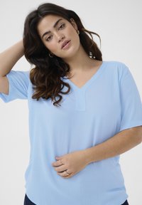 Haut bleu clair à col en V en matériau doux avec des manches courtes. Présente une finition texturée et une coupe décontractée. Conception simple et polyvalente.