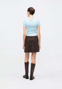 Light blue fitted short-sleeve top, brown tiered mini skirt, knee-high brown leather boots with a side zipper and accent hardware.