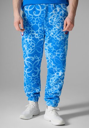 Blue fleece sweatpants with white abstract floral patterns, elastic cuffs, worn with white lace-up sneakers.