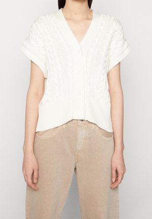 Valkoinen neulekortti, jossa on V-pääntie, lyhyet hihat ja palmikkokuvio. Varustettu nappilistalla ja ribbireunalla. Yhdistetty vaaleisiin housuihin.