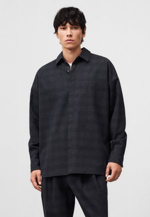 Chemise à boutons gris foncé avec col, coupe décontractée et manches longues. Le tissu texturé présente un motif subtil.