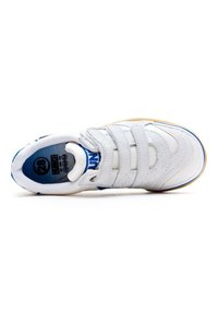 Zapatilla blanca con detalles en azul, tres correas de velcro, paneles texturizados y una suela de goma. La etiqueta interior muestra la talla 28.