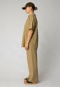 Khakifarbene, oversized Bluse und passende, weit geschnittene Hose aus leichtem Material, kombiniert mit einer dunkelgrünen Kappe und schwarzen Plateausandalen.