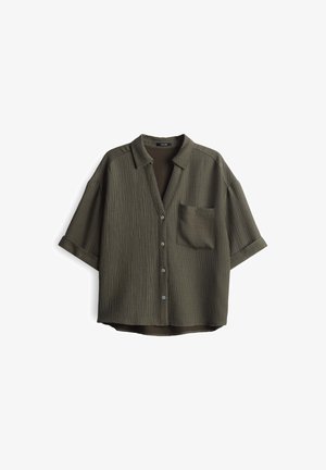 Dunkelolivgrünes Kurzarmhemd mit gerippter Textur, Knopfleiste vorne und einer einzelnen Brusttasche. Lockere Passform mit umgeschlagenem Kragen.