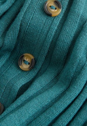 Türkiser Strickcardigan mit gerippter Textur, ausgestattet mit großen runden braunen Knöpfen in verschiedenen Farbtönen, die einen visuellen Kontrast und Details schaffen.