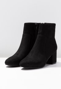 Botines de ante negros con tacón cuadrado, cierre de cremallera y textura suave. Presentan un diseño de punta afinada y costuras mínimas.