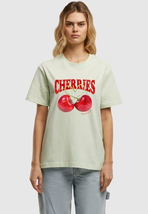 Hellgrünes T-Shirt mit einer Grafik von zwei roten Kirschen mit grünen Stielen, darüber in fettem Rot der Text "KIRSCHEN". Kurze Ärmel, runder Halsauschnitt.