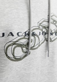 Jasnoszary materiał bluzy z kapturem z czarną i oliwkową grafiką w wzór łańcucha oraz częściowym tekstem "JACK & JONES", szare sznurki wiszące na środku z przodu.
