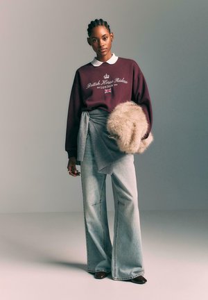 Maroon sweatshirt with white collar and branding, paired with light blue wide-leg jeans. Holding a beige fur accessory. Smooth textures.