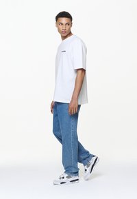White short-sleeve T-shirt with a small black logo, paired with light blue denim jeans and black-and-white sneakers. Minimalist design.