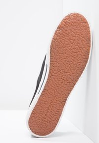 Czarne sneakersy z teksturowaną, brązową gumową podeszwą, białymi akcentami na pięcie i bokach oraz gładką, materiałową cholewką.