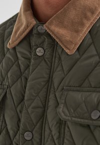 Gesteppte dunkelgrüne Jacke mit einem beigen Cordkragen. Verfügt über Metallknöpfe und eine aufgesetzte Tasche, die ein strukturiertes, isoliertes Design betont.