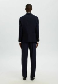 Granatowa marynarka garniturowa o dopasowanym kroju i pojedynczym rozcięciu z tyłu, zestawiona z pasującymi spodniami. Elementy ozdobne to złote guziki oraz biała koszula wizytowa.