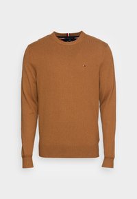 Brun stickad crew neck-tröja med långa ärmar. Har ribbade muddar och fåll, liten logga på bröstet, mjuk textur och medeltjocklek.